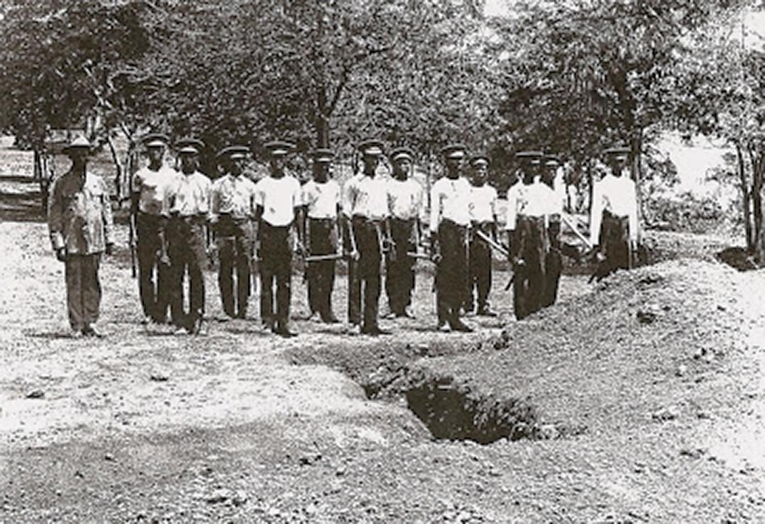 Black and white photograph showing troops of the BWIR next to a trench 