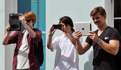 Three people are holding up tablets and a phone to view the building opposite