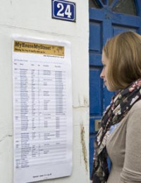 Photo of a woman reading a poster affixed to the front wall of a house